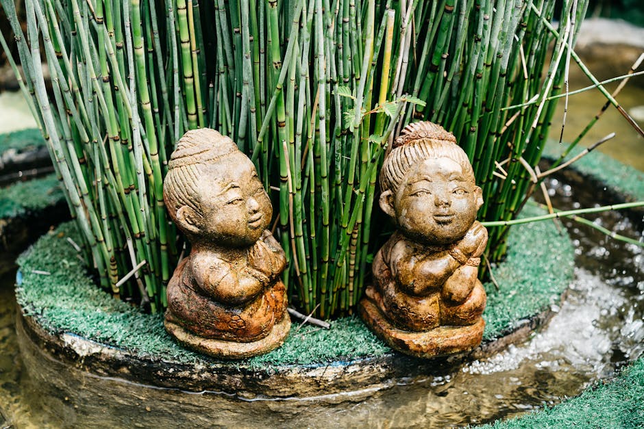 Serene garden scene with carved stone figurines, bamboo, and water feature.