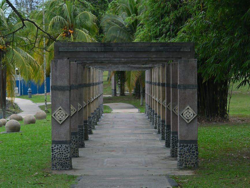 A serene stone pergola walkway surrounded by palm trees and greenery in a tropical park.
